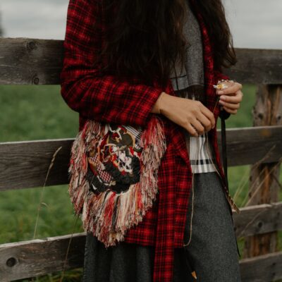 Photo by cottonbro studio A woman in boho attire with an embroidered bag leaning on a wooden fence outdoors.
