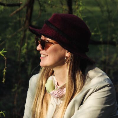 A woman in sunglasses and hat smiling outdoors, embracing the natural setting.